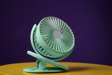 Photo of Modern electric fan on yellow table against violet background