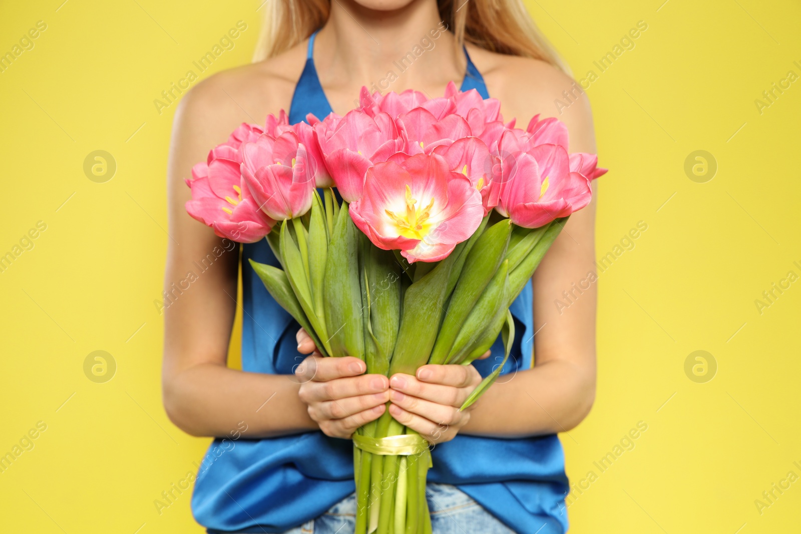 Photo of Beautiful girl with spring tulips on yellow background, closeup. International Women's Day