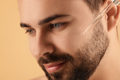 Photo of Handsome man applying cosmetic serum onto face, closeup