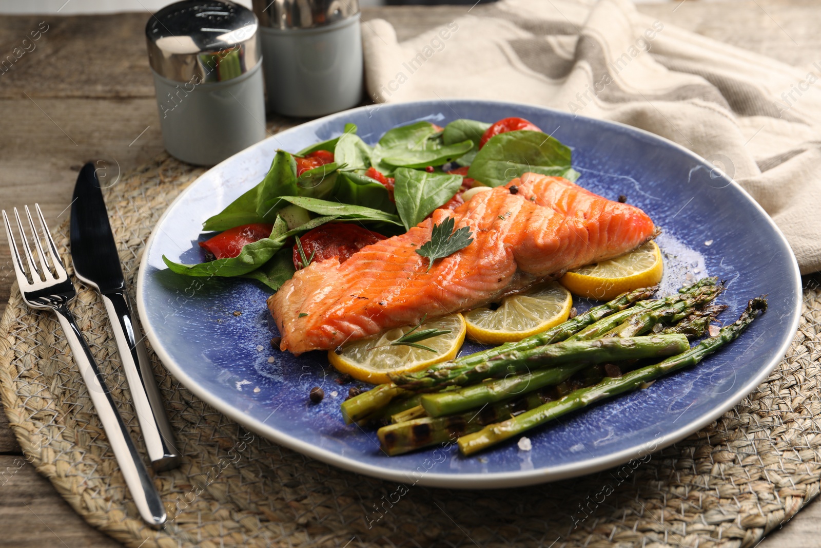 Photo of Tasty grilled salmon with tomatoes, asparagus, spinach and lemon served on table, closeup