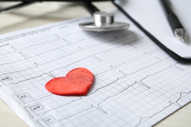 Photo of Cardiogram report, red decorative heart and stethoscope on table, closeup
