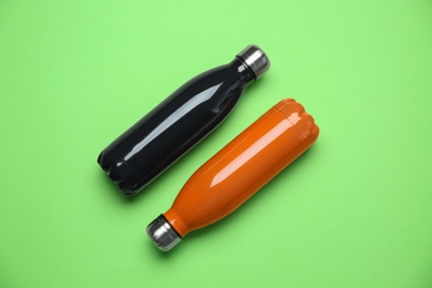 Photo of Different thermo bottles on green background, flat lay