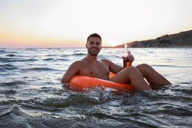 Happy young man with drink on inflatable ring in water