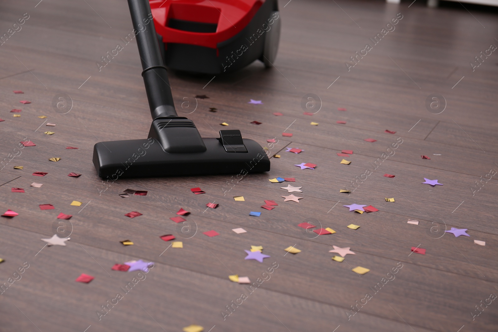 Photo of Vacuuming confetti from wooden floor in room