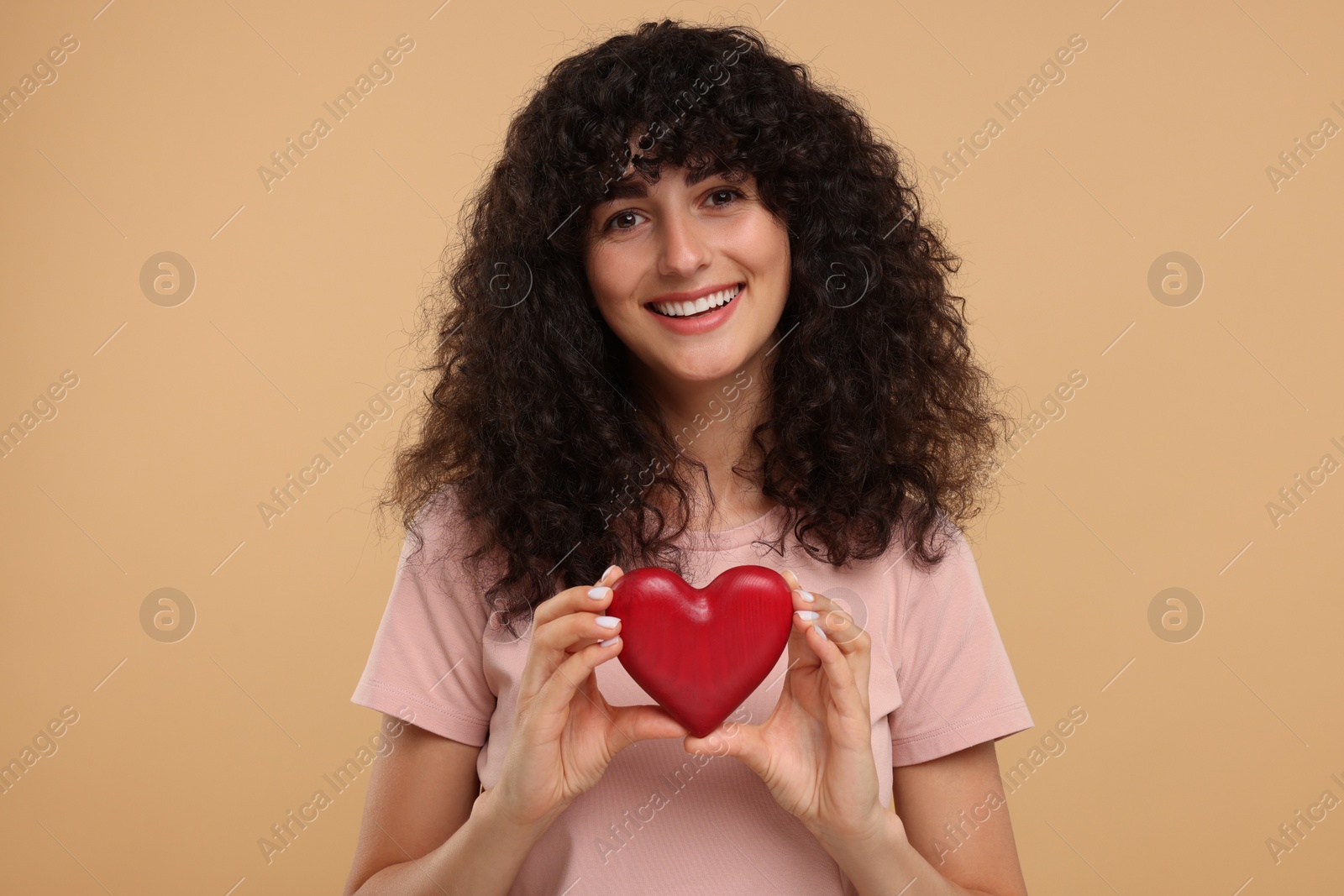 Photo of Happy young woman holding decorative red heart on beige background