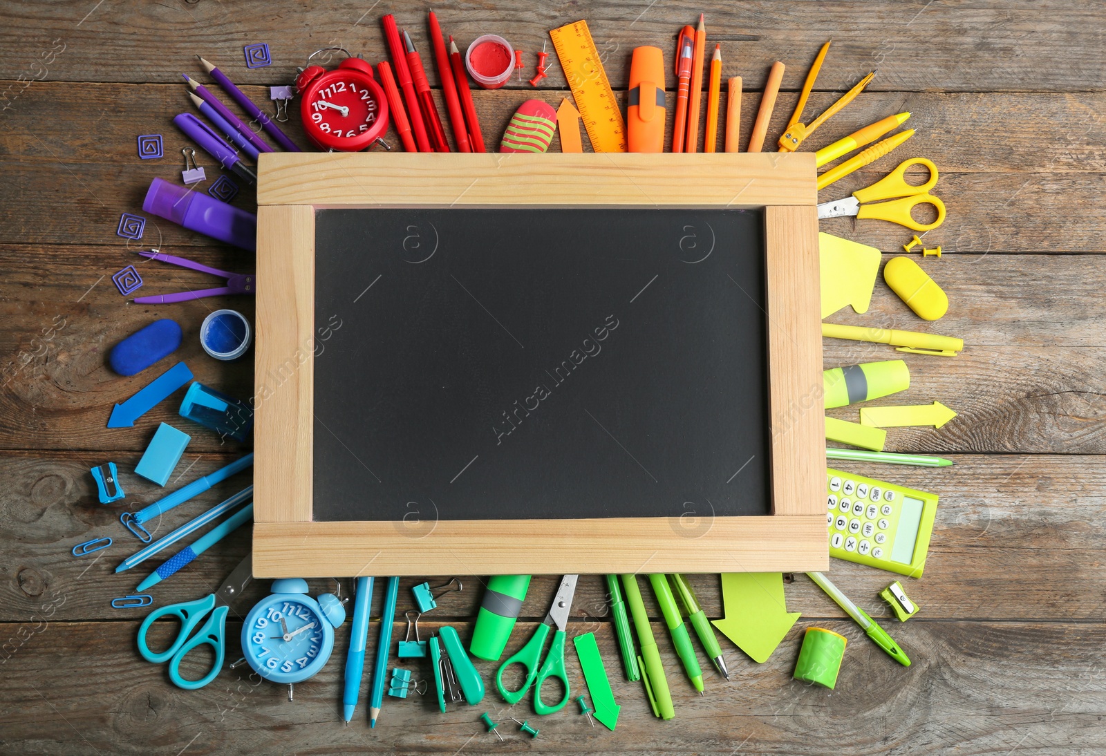 Photo of Different school stationery and blank small chalkboard on wooden background, flat lay. Space for text
