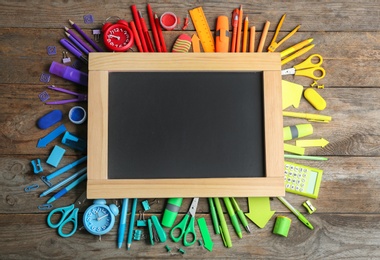 Different school stationery and blank small chalkboard on wooden background, flat lay. Space for text