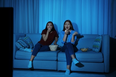 Photo of Friends with bowl of popcorn watching TV together on sofa in dark living room