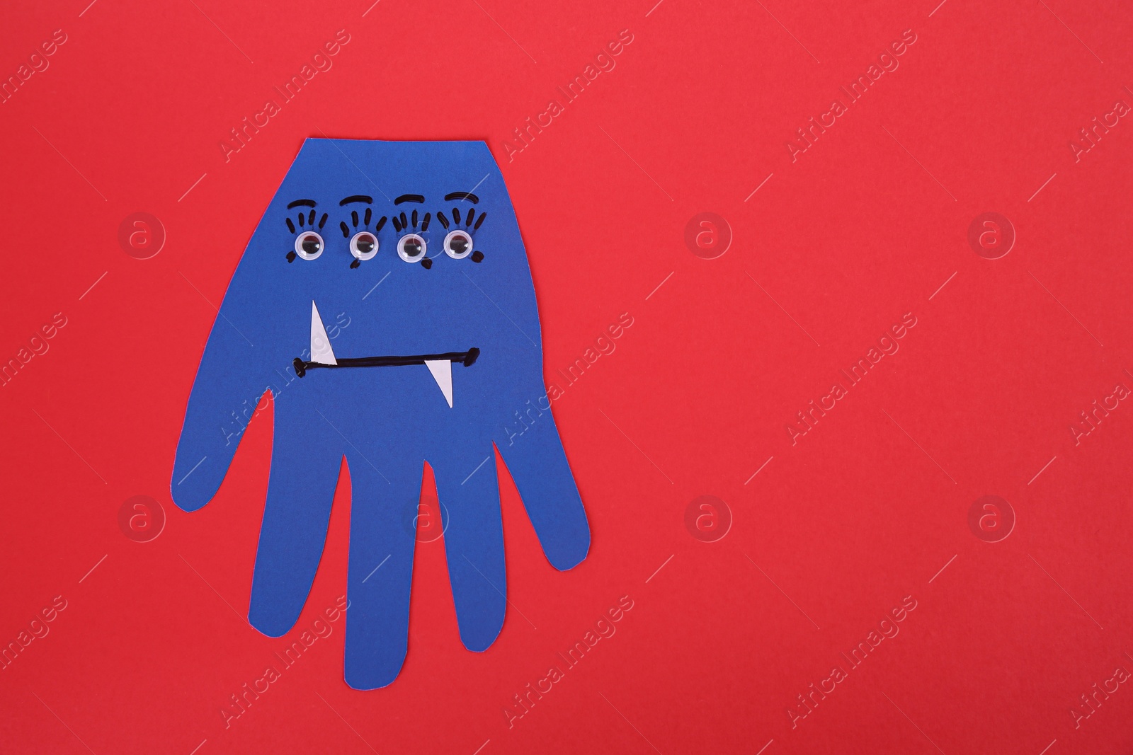 Photo of Funny blue hand shaped monster on red background, top view with space for text. Halloween decoration