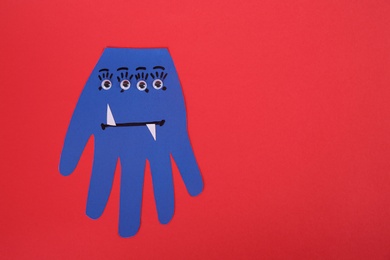 Photo of Funny blue hand shaped monster on red background, top view with space for text. Halloween decoration