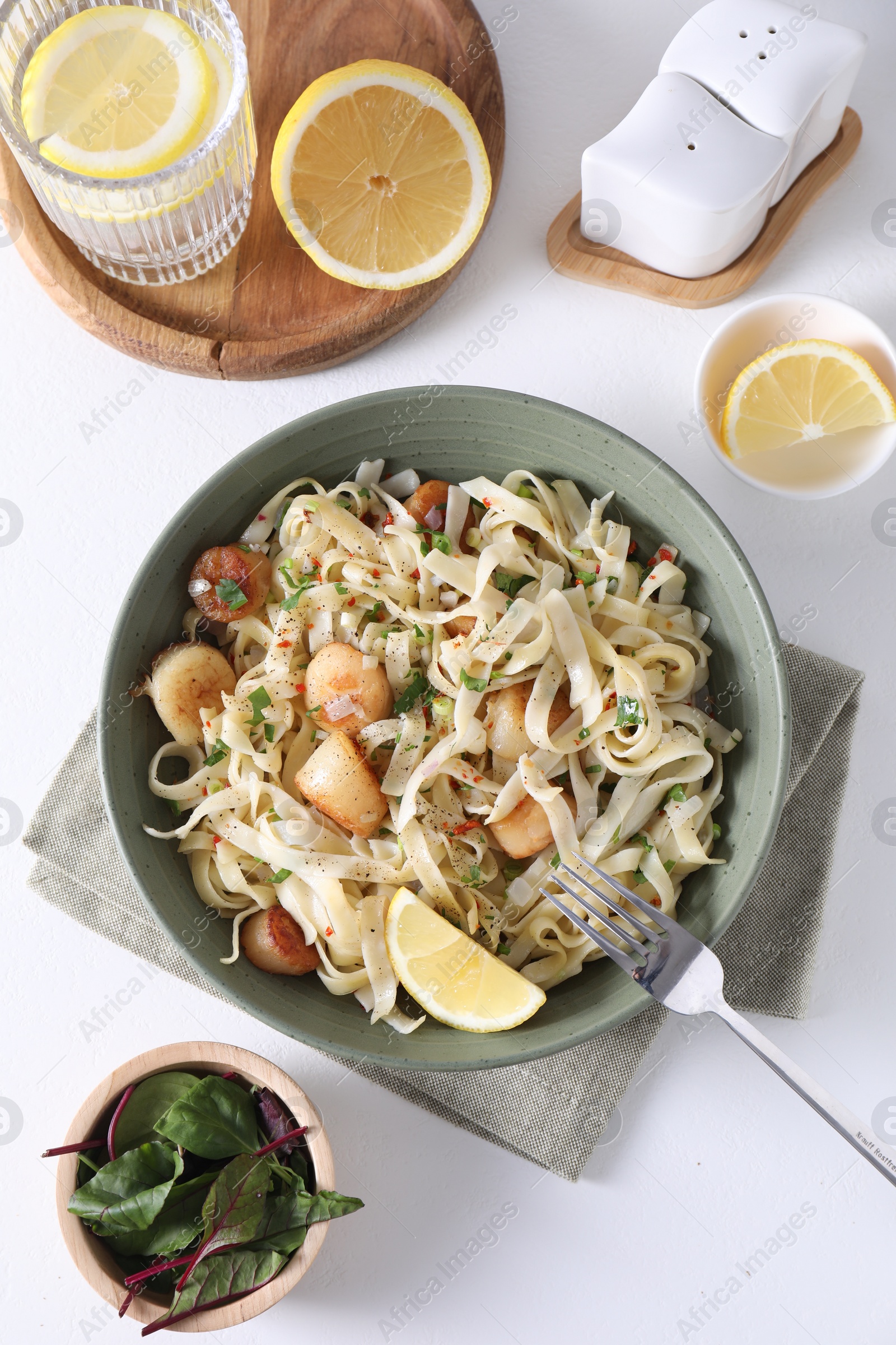 Photo of Delicious scallop pasta with spices and lemon in bowl served on white table, flat lay