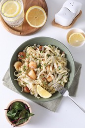 Delicious scallop pasta with spices and lemon in bowl served on white table, flat lay