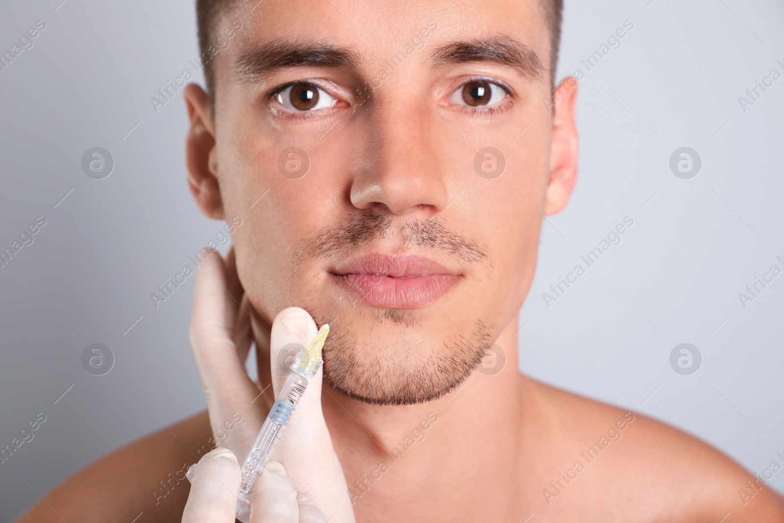 Photo of Man getting facial injection on grey background, closeup. Cosmetic surgery