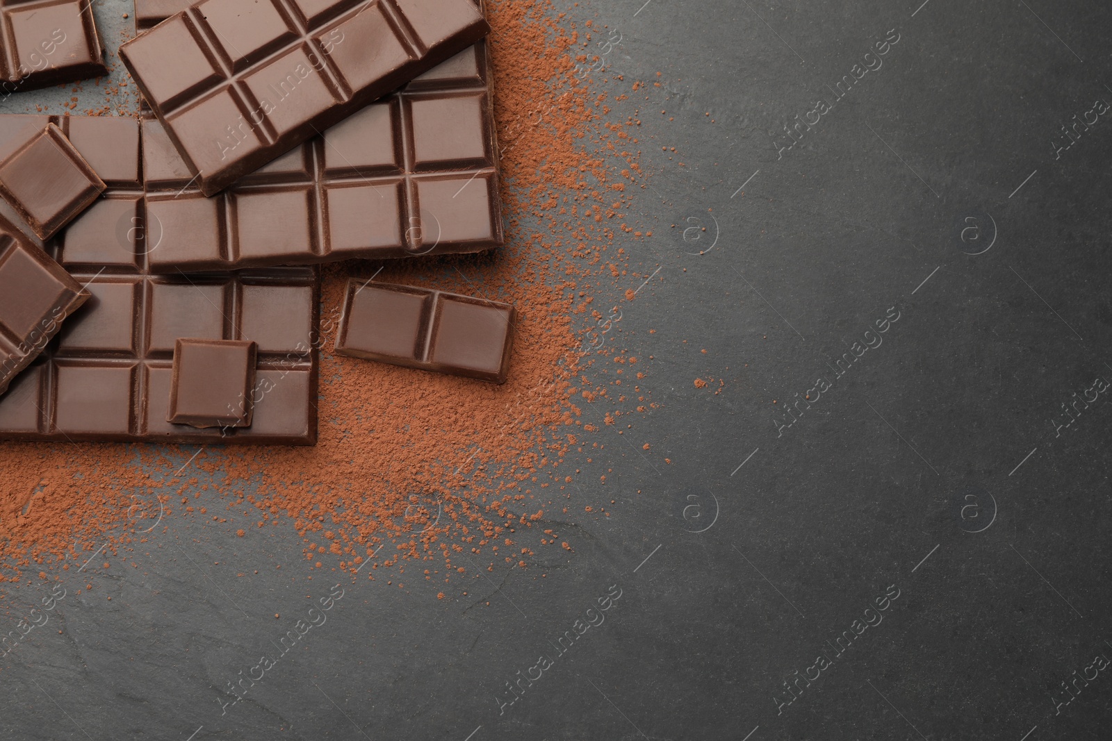 Photo of Delicious dark chocolate and cocoa powder on black table, flat lay. Space for text