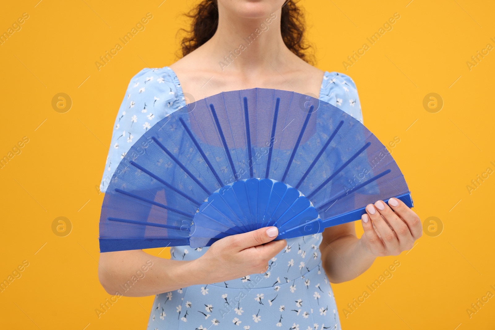 Photo of Woman holding hand fan on orange background, closeup