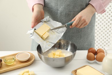 Photo of Woman adding fresh butter into bowl with flour at white table, closeup