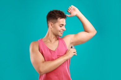 Young man applying deodorant to armpit on blue background