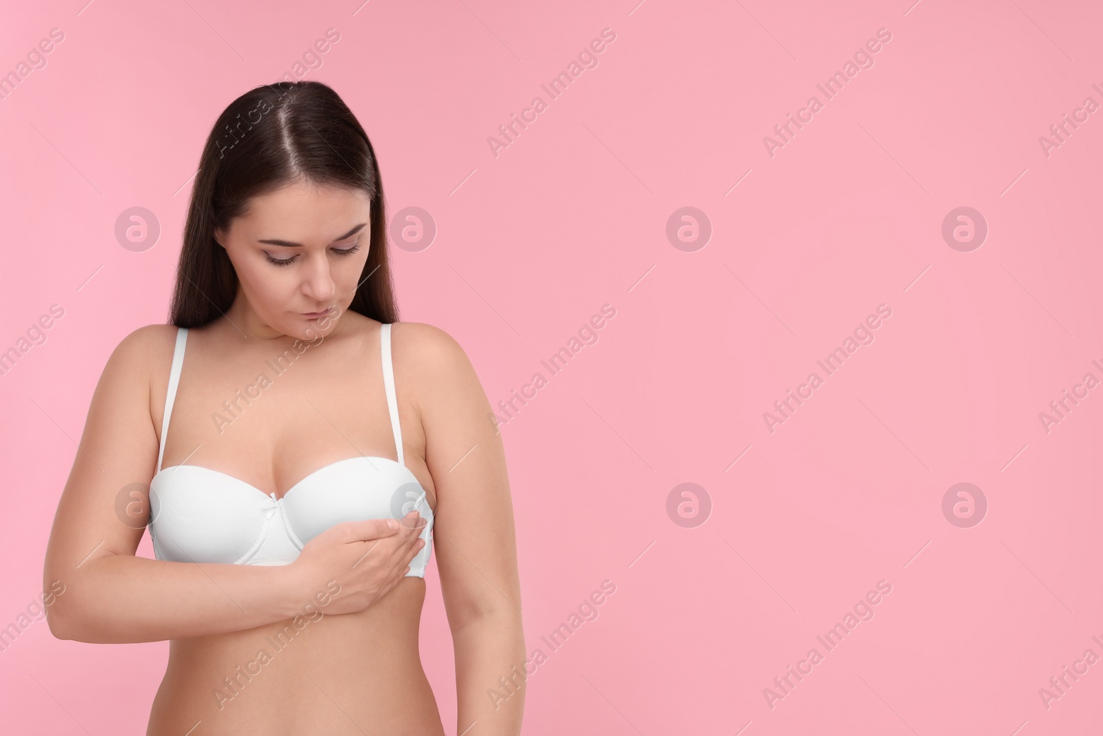 Photo of Mammology. Woman in bra doing breast self-examination on pink background, space for text