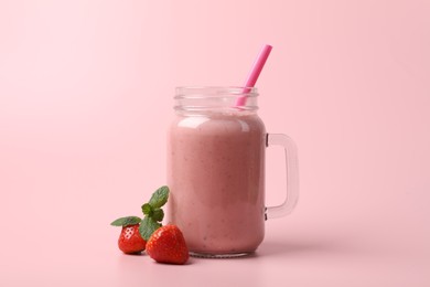 Photo of Mason jar with delicious berry smoothie and fresh strawberries on pink background