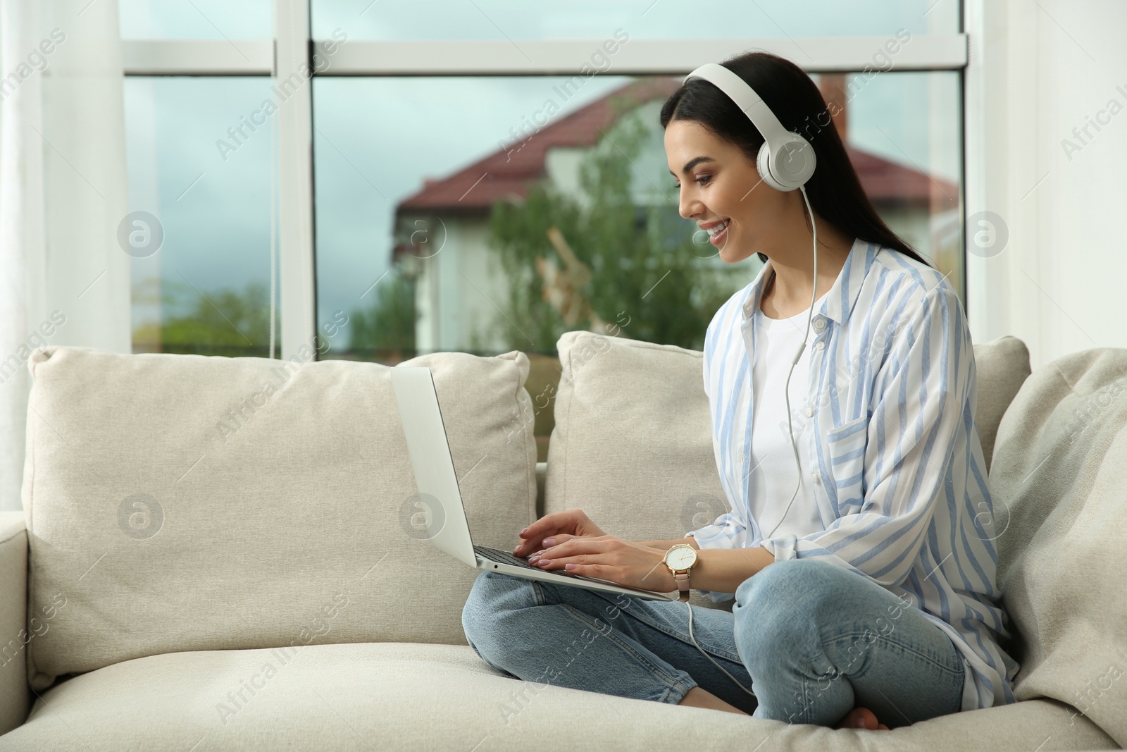 Photo of Young woman with laptop and headphones on sofa at home, space for text