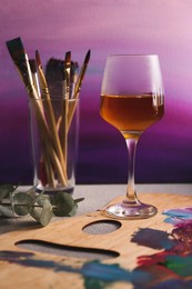 Photo of Wooden artist's palette with colorful paints and glass of wine on grey table