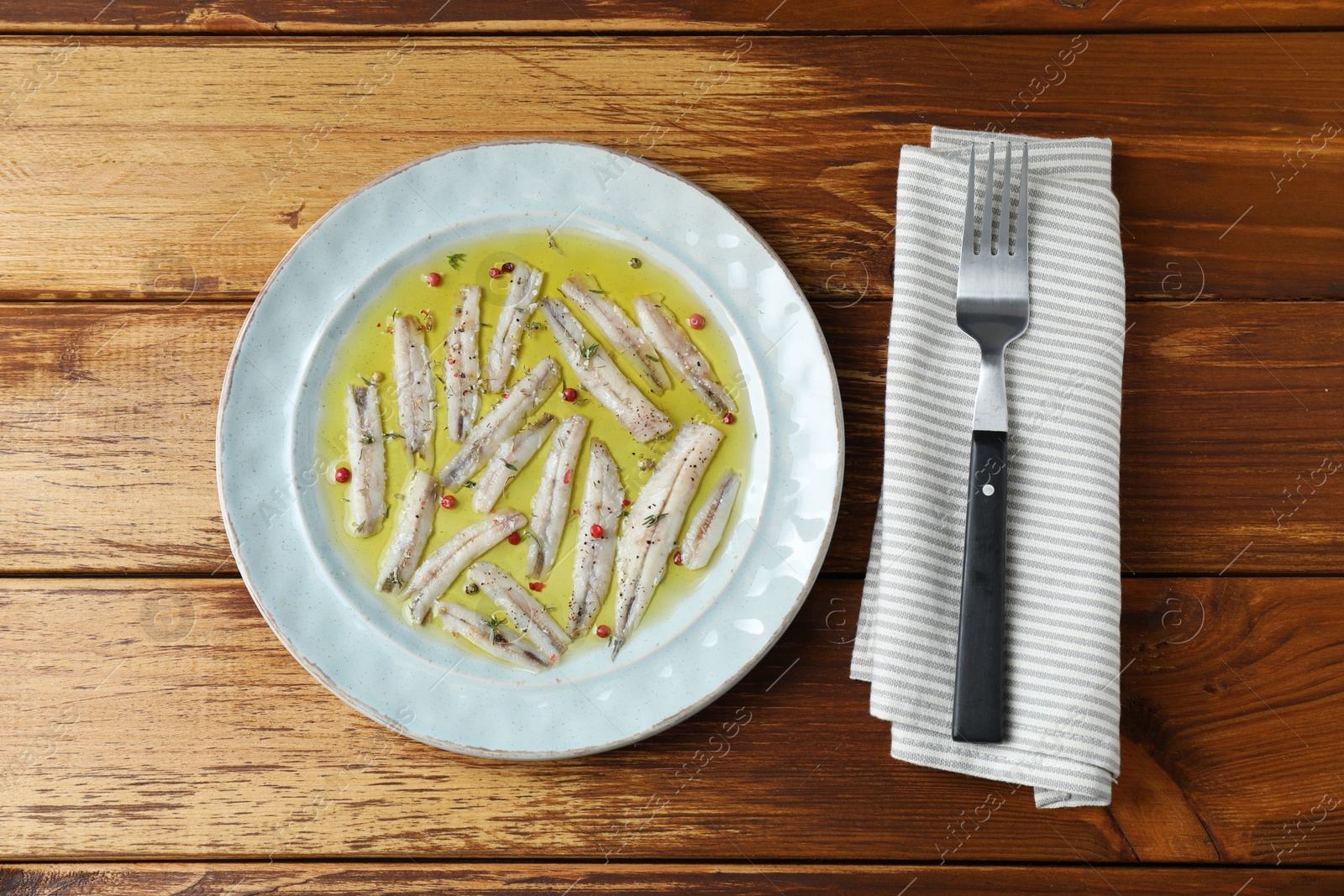 Photo of Tasty pickled anchovies with spices on wooden table, top view