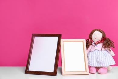 Photo of Photo frames and adorable doll on table against color background, space for text. Child room elements