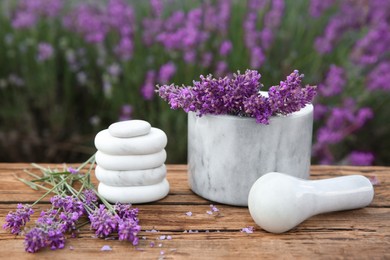 Photo of Spa stones, fresh lavender flowers and white marble mortar on wooden table outdoors, closeup