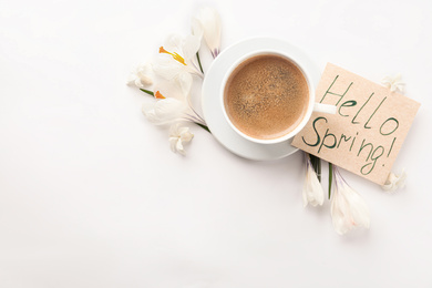 Card with words HELLO SPRING, cup of coffee and fresh flowers on white background, flat lay. Space for text