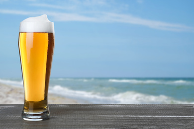 Image of Cold beer on wooden desk against blurred sea. Space for text