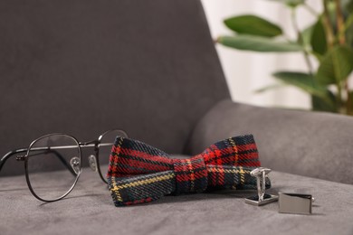 Stylish tartan bow tie, glasses and cufflinks on grey armchair