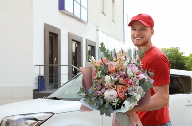 Delivery man with beautiful flower bouquet near car outdoors