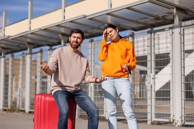 Photo of Being late. Worried couple with red suitcase outdoors
