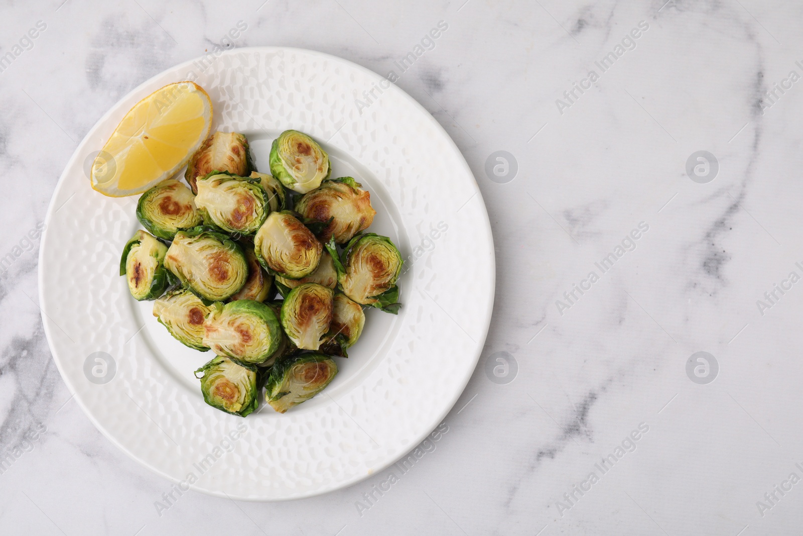 Photo of Delicious roasted Brussels sprouts and slice of lemon on white marble table, top view. Space for text