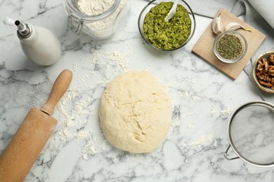 Photo of Making delicious pesto bread. Raw dough and ingredients on white marble table, flat lay