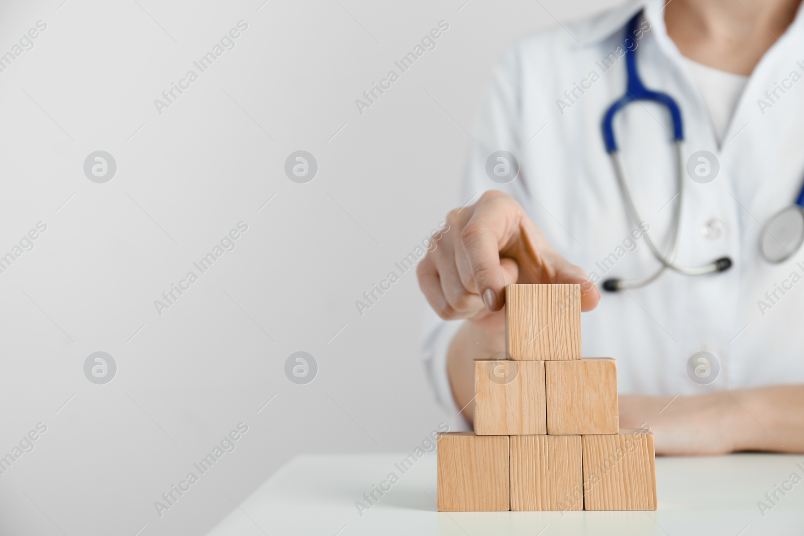 Photo of Doctor building pyramid of blank wooden cubes on white table against light background, closeup. Space for text