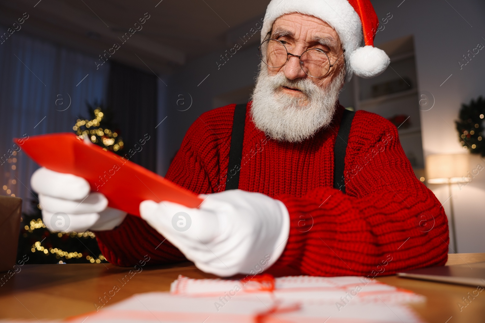 Photo of Santa Claus holding letter at his workplace in room decorated for Christmas