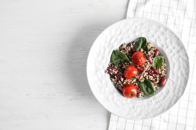 Plate with healthy quinoa salad and vegetables on wooden table, top view. Space for text