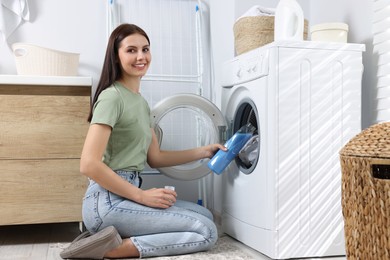 Photo of Woman pouring fabric softener into washing machine in bathroom, space for text