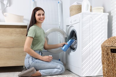 Woman pouring fabric softener into washing machine in bathroom, space for text