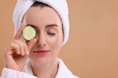 Photo of Beautiful woman covering eye with piece of cucumber on beige background, closeup. Space for text