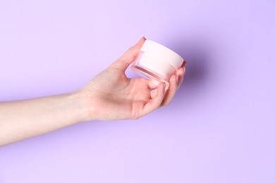 Woman holding jar of cream on violet background, closeup