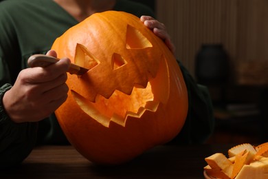 Woman carving pumpkin for Halloween at wooden table indoors, closeup