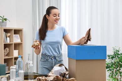 Photo of Garbage sorting. Smiling woman throwing crumpled paper into cardboard box in room