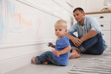 Photo of Upset father watching his little son drawing on wall at home