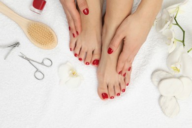 Photo of Woman with stylish red toenails after pedicure procedure, tools and orchid flowers on white terry towel, top view