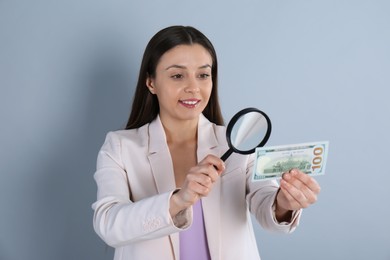 Photo of Expert authenticating 100 dollar banknote with magnifying glass on light grey background. Fake money concept