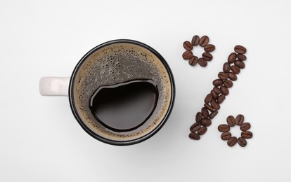 Cup of coffee and beans as percent sign on white background, top view. Decaffeinated drink