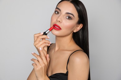 Photo of Young woman applying red lipstick on light gray background