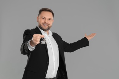 Male real estate agent holding key on grey background